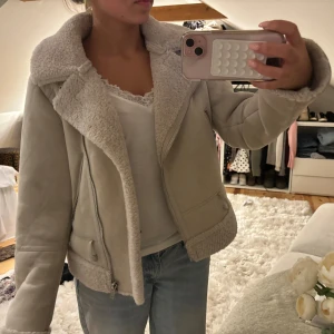 Beige teddyjacka med dragkedja - Snygg beige teddyjacka med stora kragar och mysigt foder. Jackan har dragkedja framtill och detaljer i samma färg. Perfekt för dig som vill ha en varm och trendig look med lite oversized känsla.