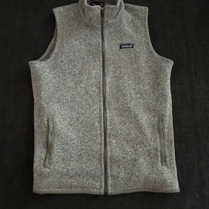 Grå fleeceväst från Patagonia - Säljer en grå fleeceväst från Patagonia i storlek L men passar mer M.Västen har hel dragkedja framtill, två sidofickor med dragkedja och en mjuk, stickad yta. Perfekt för lager-på-lager och chill dagar. Diskret Patagonia-logga på bröstet.