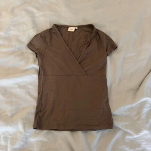 Brun omlottopp  - Säljer en brun omlottopp från Nelly i storlek S. Toppen har korta ärmar, v-ringning och är tillverkad i mjuk bomull. Basic men med detaljer🤎- läs min bio för information 💌