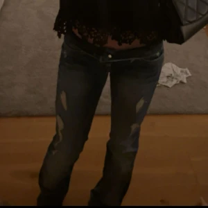 Blå slitna bootcut jeans - Säljer ett par blå jeans med slitningar framtill och klassisk femficksdesign. Jeansen har bootcut-modell och låg midja, med snyggt tvättad denim och detaljerade sömmar. Perfekta för dig som gillar en avslappnad och trendig look.