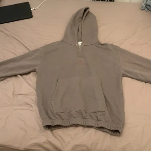 Grönish hoodie med half zip från Zara - Mysig grå hoodie från Zara med huva och praktisk half zip-dragkedja framtill. Tröjan har en stor känguruficka och elastisk nederkant. Perfekt för chill dagar och enkel att matcha med jeans eller mjukisbyxor.