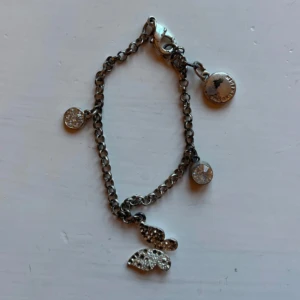 Snyggt silverfärgat armband med berlocker - Stilrent armband i silverfärg med flera glittriga berlocker, bland annat en fjäril och runda hängen med stenar. Kedjan är klassisk och har en smidig karbinlås. Perfekt för dig som gillar detaljer och vill ha något som sticker ut lite extra.
