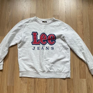 Vit sweatshirt från Lee Jeans - Vit sweatshirt från Lee Jeans med stort tryck i rött och blått framtill. Tröjan är storlek L men är väldigt liten i storleken så den sitter mer lik S/M.