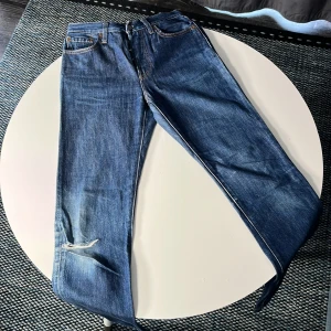 Levi's Premium blå jeans W25 L30 - Säljer ett par klassiska Levi's Premium jeans i blå denim med raka ben och snyggt slitna detaljer vid knät. Jeansen har fem fickor, orange sömmar och knappgylf. Perfekt för dig som gillar en tidlös och avslappnad look.