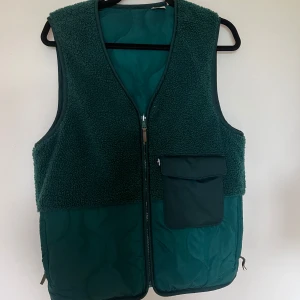 Mörkgrön fleeceväst med ficka - Mysig mörkgrön väst i fleece med quiltad nederdel och stor ficka framtill med lock. Västen har dragkedja hela vägen och en enkel, rak passform.  Från Levis🥰🥰