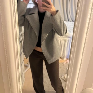 Grå ulljacka från Bubbleroom x Lojsan Wallin - Snygg grå jacka i ullmix från Bubbleroom x Lojsan Wallin. Jackan har bred krage, asymmetrisk dragkedja och två fickor framtill. Perfekt för höst och vinter, med en loose fit och stilren look.