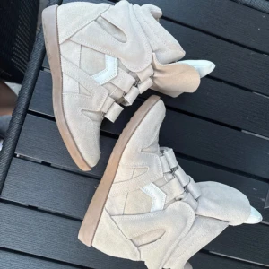 Beige Isabel Marant wedge sneakers - Säljer ett par ikoniska beige wedge sneakers från Isabel Marant i beige med vita detaljer. Storlek 36 passar på 37. De har 5 cm klack. 