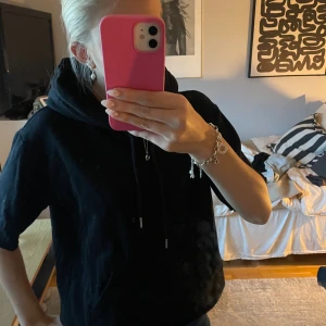 Svart hoodie med kort ärm - Säljer en svart hoodie med korta ärmar och huva. Tröjan har snörning i halsen och en avslappnad passform, perfekt för en chill och stilren look. Passar lika bra till jeans som till mjukisbyxor. (Har själv klippt av ärmarna)