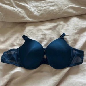 Mörkblå bh  - Säljer en mörkblå bh från Primark med släta kupor och justerbara axelband. Sidorna har meshdetaljer och bh:n har klassisk knäppning bak. Enkel och stilren design som passar till det mesta.
