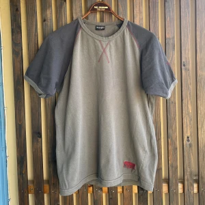 Ringer tee från Wrangler, storlek L - Säljer en t-shirt från Wrangler med mörkare grå raglanärmar och röda kontrastsömmar. T-shirten har rund halsringning och en broderad Wrangler-logga nertill. Skön och avslappnad passform, perfekt till jeans. 
