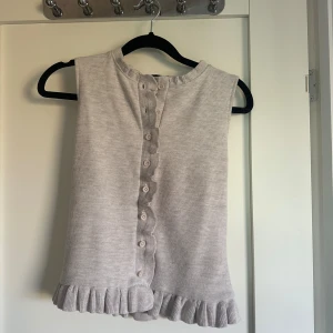 Beige ärmlös linnetopp med volang - Supersöt beige linnetopp med knappar framtill och volangdetaljer längs knappslån och nederkanten. Säljer även den i grått. 