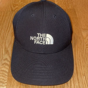Svart keps från The North Face - Snygg svart keps från The North Face med klassisk böjd skärm och broderad logga framtill i vitt. Kepsen har ventilerande hål och justerbar passform. Perfekt accessoar för en sportig och stilren look. PRIS KAN DISKUTERAS VID SNABB AFFÄR