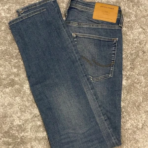Blå jeans från Jack & Jones - Säljer ett par klassiska blå jeans från Jack & Jones med fem fickor och snygga sömdetaljer på bakfickan. Jeansen har en rak passform och är tillverkade i mjukt denimtyg som sitter skönt hela dagen.