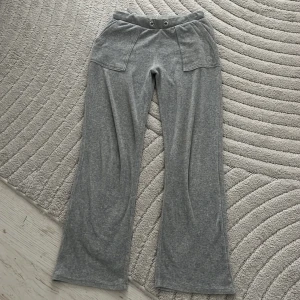 Grå mjukisbyxor Juicy Couture - Grå mjukisbyxor från Juicy Couture med bred resår i midjan och två stora fickor framtill. Byxorna har ett broderat JC-logo på ena fickan och vida ben. Perfekta för en chill och avslappnad stil. (snörren saknar⚠️⚠️) storlek 12/13 men funkar för xs/s