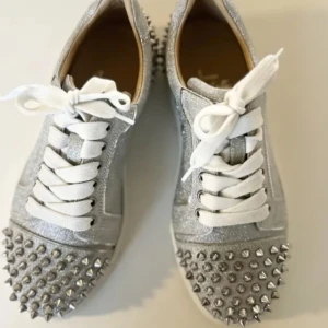 Glittriga looubs - Snygga silverglittriga sneakers från Christian Louboutin med nitar på tån och hälen. Skorna har vita snören och en rund tå. Perfekta för att ge din outfit en edgy touch. De är lite slitnare än på bilden och en nit som saknas.