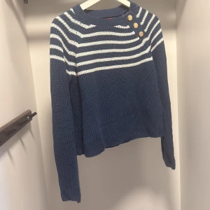 Randig blå stickad tröja från Guess - Säljer en blå och vit randig stickad tröja från Guess i storlek XS. Tröjan har lång ärm, rund halsringning och tre snygga guldknappar på axeln. Perfekt för dig som gillar klassisk stil med en twist.