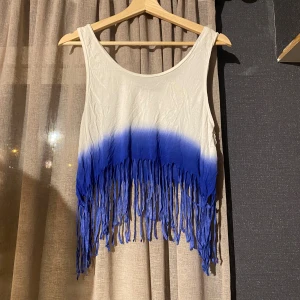 Vit och blå fransig linnetopp BikBok - Säljer en cool ärmlös linnetopp från BikBok i storlek XS. Toppen är vit upptill och övergår i blått nertill med långa fransar längs nederkanten. Perfekt för sommarens festivaler eller strandhäng.