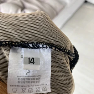 Svart glittrig dansklänning med mesh - Supersnygg svart konståkningsklänning med transparent mesh upptill och långa ärmar. Klänningen har massor av svarta och guldiga paljetter, hög krage och öppen rygg. Kjolen är kort och har ett lätt fall. Perfekt för dig som vill sticka ut på isen! Knappt använd.