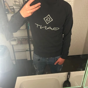 Svart sweatshirt från Gant - Svart sweatshirt från Gant med vit broderad logga på bröstet. Klassisk rund halsringning och långa ärmar. Perfekt för dig som gillar stilrena och bekväma plagg med tydlig logga.