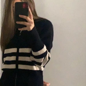 Randig svart hoodie med dragkedja - Trendig zara tröja Säljer en svart ribbstickad hoodie med vita ränder och dragkedja framtill. Tröjan har huva och långa ärmar, samt en croppad passform som ger en snygg och modern look. Perfekt för dig som gillar streetstyle och vill ha något bekvämt men ändå trendigt.