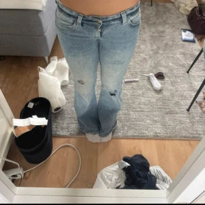 Bootcut ljusblå jeans med slitningar - Säljer ett par ljusblå bootcut jeans med slitningar och hål på låren. Jeansen har klassisk femficksmodell, låg midja och är tillverkade i denim. Perfekta för dig som gillar en avslappnad och trendig look. Inte mina bilder❤️