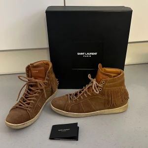 Saint Laurent bruna mocka sneakers med fransar - Saint Laurent SL-18 Fringe High “Tan” Storlek 39 EU Köpta begagnade. Skosnörena har gått sönder lite, ett av dem är utbytt mot ett originalskosnöre. Supercoola och unika sneakers i mocka från Saint Laurent   #saintlaurent #ysl #saintlaurentsneakers #sl18 #fringehigh #designerfashion #luxurystyle #vintedsweden #vintedsverige #sneakerslover #streetstyle #fashionfinds #secondhandfashion #sustainablefashion #vintagefashion #tan #mockaskor #sneak
