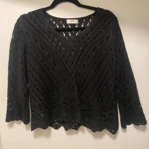 Svart tröja från JDY - Svart stickad tröja från JDY med vackert hålmönster och vågig nederkant.