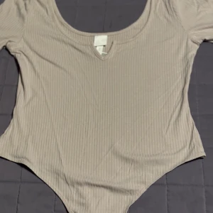 Beige ribbad bodysuit från H&M - Säljer en beige ribbad bodysuit från H&M i storlek M. Den är helt oanvänd och som ny.