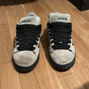 Adidas sneakers i grå mocka - Snygga Adidas sneakers i grå mocka med svarta detaljer och klassiska tre ränder på sidan. Skorna har svart platt sula och breda svarta snören. Låg modell med rund tå och Adidas-logga på plösen och hälen. 1100kr nya knappt slitna på under sidan 