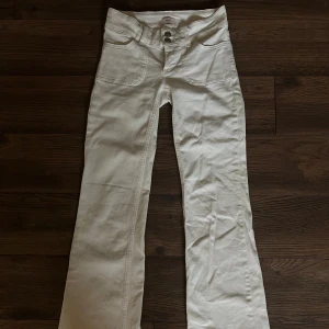 Vita bootcut jeans från Nelly - Snygga vita jeans från Nelly med bootcut passform. Byxorna har låg midja, stora framfickor och bakfickor med lock och silverfärgade knappar. Tillverkade i ett stretchigt bomullsmaterial som sitter skönt och ger en clean look.