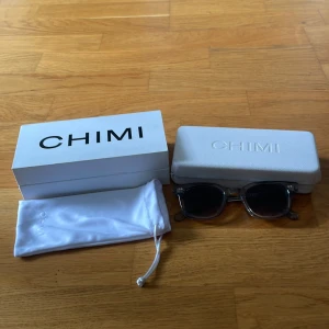 Grå transparenta CHIMI solglasögon - Snygga solglasögon från CHIMI med transparent grå båge och mörka glas. Modellen har en klassisk, något fyrkantig form och coola detaljer i metall på skalmarna. Kommer med originalfodral och tygpåse. Perfekt accessoar för att lyfta din stil.