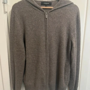 Brun kashmir hoodie från Lawrence Grey - Mysig brun hoodie från Lawrence Grey i 100% kashmir. Tröjan har dragkedja framtill, huva och två fickor. Perfekt för dig som gillar en clean och stilren look med lyxig känsla. Långärmad och i normal passform. Fast pris 