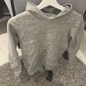 Grå hoodie från Ahlquist Clothing XS - Mysig grå hoodie från Ahlquist Clothing i storlek XS. Tröjan har en klassisk huva och är tillverkad i ett mjukt stickat material. Perfekt för kyliga dagar och enkel att matcha med jeans eller mjukisbyxor. Kashmir hoodie från ahlqvist clothing. Tvättad så att den blev mindre. Förut var den S nu är den XS.