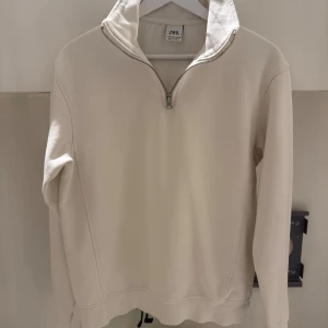 Beige half zip tröja från Zara - Säljer en stilren beige långärmad tröja från Zara med hög krage och half zip-dragkedja. Tröjan är i mjuk bomull och har en clean look utan mönster eller tryck. Perfekt för lager-på-lager och chill dagar.