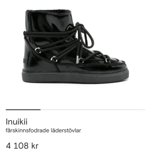Svarta Inuikii fårskinnsstövlar - Säljer ett par svarta Inuikii stövlar med glansig finish och grova snören runt hela skon. Insidan är fodrad med mjukt fårskinn för extra värme. Yttermaterialet är läder och sulan är platt och robust. Perfekt för dig som vill ha både stil och komfort under kalla dagar.