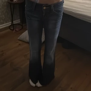 Mörkblå bootcut jeans från Cheap Monday - Säljer ett par mörkblå jeans från Cheap Monday med riktigt breda bootcut-ben och klassisk femficksdesign. Jeansen har låg midja och coolt Cheap Monday-märke med döskalle bak. Perfekt för dig som gillar retrovibbar och statement-plagg.