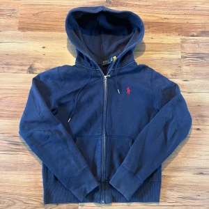 Marinblå zip hoodie från Polo Ralph Lauren - Marinblå zip hoodie från Ralph Lauren XS 🐎         - Längd (55 cm), bredd (45cm), ärm (61cm)       8/10 skick, inga skador, lite smutsig bara, finns qr kod för äktenskapsbevis                        Hör av er 🫡