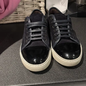 Lanvins - Snygga mörkblå sneakers från Lanvin med ovandel i mocka och detaljer i skinn. Tåpartiet är i svart lack och sulan är vit. Skorna har snörning och klassisk låg profil. Perfekta för dig som gillar stilrena och exklusiva sneakers med en twist. Dessa är köpta nya och använda 5 gånger. Uk5 och passar 40-41-42. Pris kan diskuteras vid snabb affär 