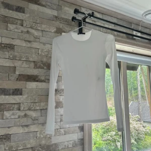 Vit långärmad tröja från Zara - Säljer en stilren vit långärmad tröja från Zara. Tröjan har en tight passform och är tillverkad i mjuk bomull, perfekt att bära som basplagg. Enkel och clean design med rund halsringning, passar till allt i garderoben.