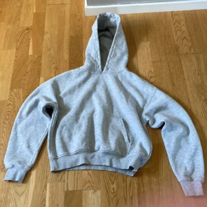 Grå hoodie från Basically Basics - En klassisk ljusgrå hoodie från Basically Basics i storlek XXS. Tröjan har huva, magficka och ribbade muddar vid ärmslut och nederkant. Perfekt för chill dagar eller när du vill ha en enkel och stilren look.