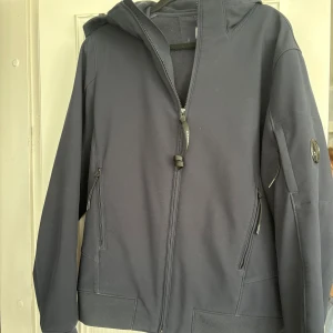 Svart vindjacka från C.P. Company - Svart vindjacka från C.P. Company med huva och dragkedja framtill