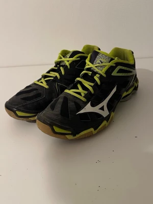 Svarta och limegröna Mizuno sneakers - Säljer ett par Mizuno Wave Lightning sneakers i svart och limegrönt med vita detaljer. Skorna har snörning, meshpaneler för ventilation och en sportig design med Mizuno-logga på sidan. Perfekta för dig som gillar att sticka ut på träningen.