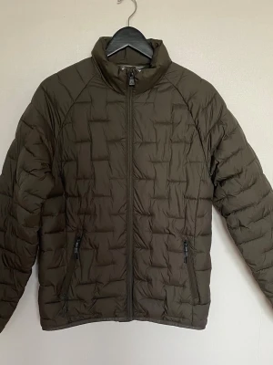Mckinley pufferjacka  - Säljer en mörkgrå McKinley pufferjacka med quiltad design och hög krage. Jackan har två sidofickor med dragkedja och en innerficka.Perfekt för kyliga dagar.Den är i nyskick och knappt använd.