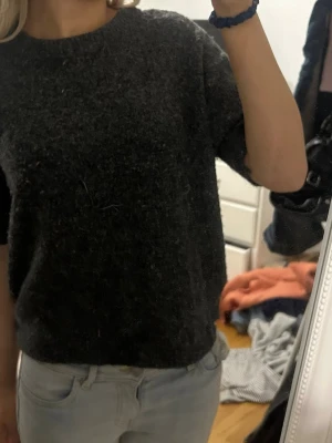 Mörkgrå stickad tröja med kort ärm - Söt kortärmad stickad tröja, köpt på vinted och har ingen lapp men har för mig att den är från hm! Tror att föra ägaren klippt av armarna och även nertill på tröjan men inget som märkts när jag använt den!