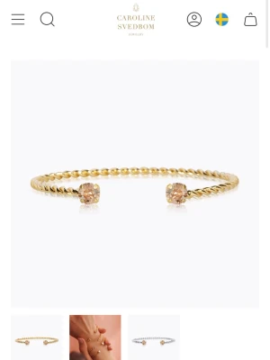 Guldarmband Caroline Svedbom - Säljer ett elegant guldarmband från Caroline Svedbom med tvinnad design och två ljusa kristaller i ändarna. Armbandet är öppet och flexibelt, perfekt för att ge en lyxig touch till din outfit.