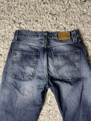 Blå jeans från Nudie Jeans - Säljer ett par nudie jeans med en sjuk wash. Jeansen har en straight fit skulle jag säga och storleken är 31/30! Säljer jeansen för 899kr, ifall ni har några funderingar är det bara att höra av er! (Defekt på bild 5)