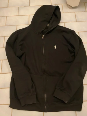 En svart polo hoodie  - Jag säljer en svart polo hoodie för den inte passar mig så bra den har en luva två små fickor och Ralph lauren märket på vänstra bröstet och är i storlek L