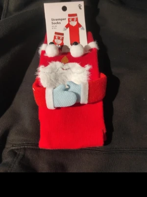 Röd julstrumpa med tomtedesign - Rolig röd strumpa från Flying Tiger med 3D-tomtedesign, fluffigt vitt skägg och blå vantar. Perfekt för att maxa julkänslan! Strumpan är gjord i mjuk polyester och har detaljer som gör den extra festlig.