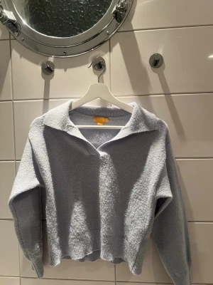 Ljusgrå stickad tröja från Gina Tricot - Supermjuk ljusgrå stickad tröja från Gina Tricot med krage och v-ringning. Tröjan har lång ärm, ribbade muddar och en lite croppad passform. Perfekt för lager på lager under kyliga dagar.