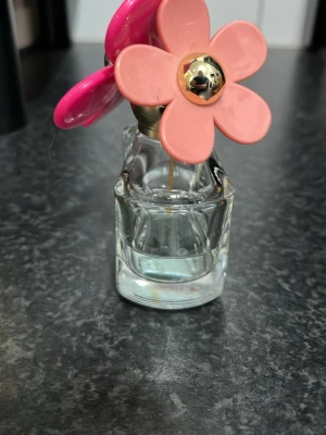 Daisy  by Marc Jacobs - Ca 50% kvar. Snygg parfym från Marc Jacobs med ikonisk blommig kork i rosa och turkost. Perfekt för dig som vill ha en trendig accessoar på sminkbordet. Flaskan har en lekfull design som sticker ut och passar dig som gillar färg och stil.